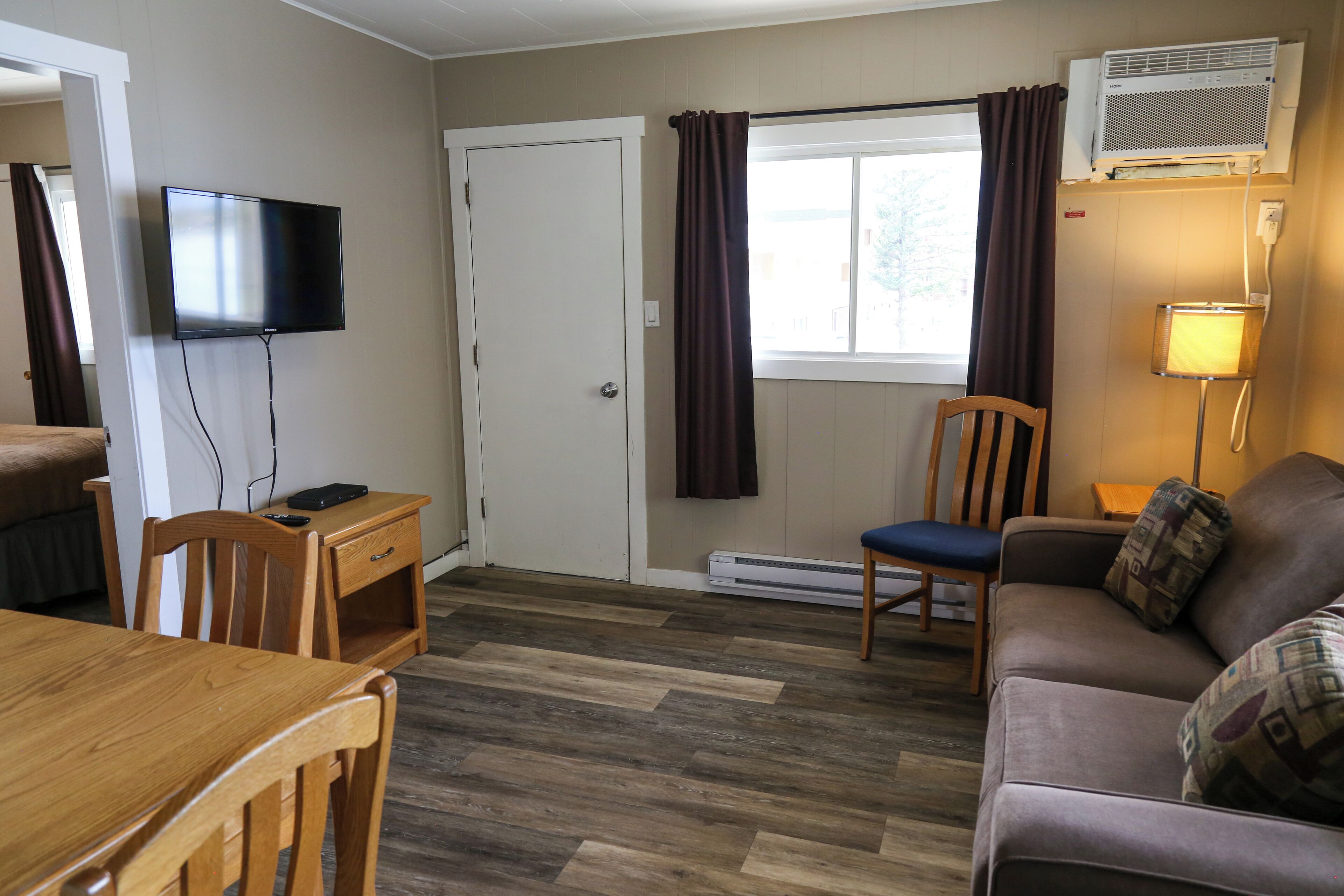 Une chambre meublée comprenant une télévision, un bureau, une chaise, un canapé, une fenêtre avec des rideaux et un radiateur.