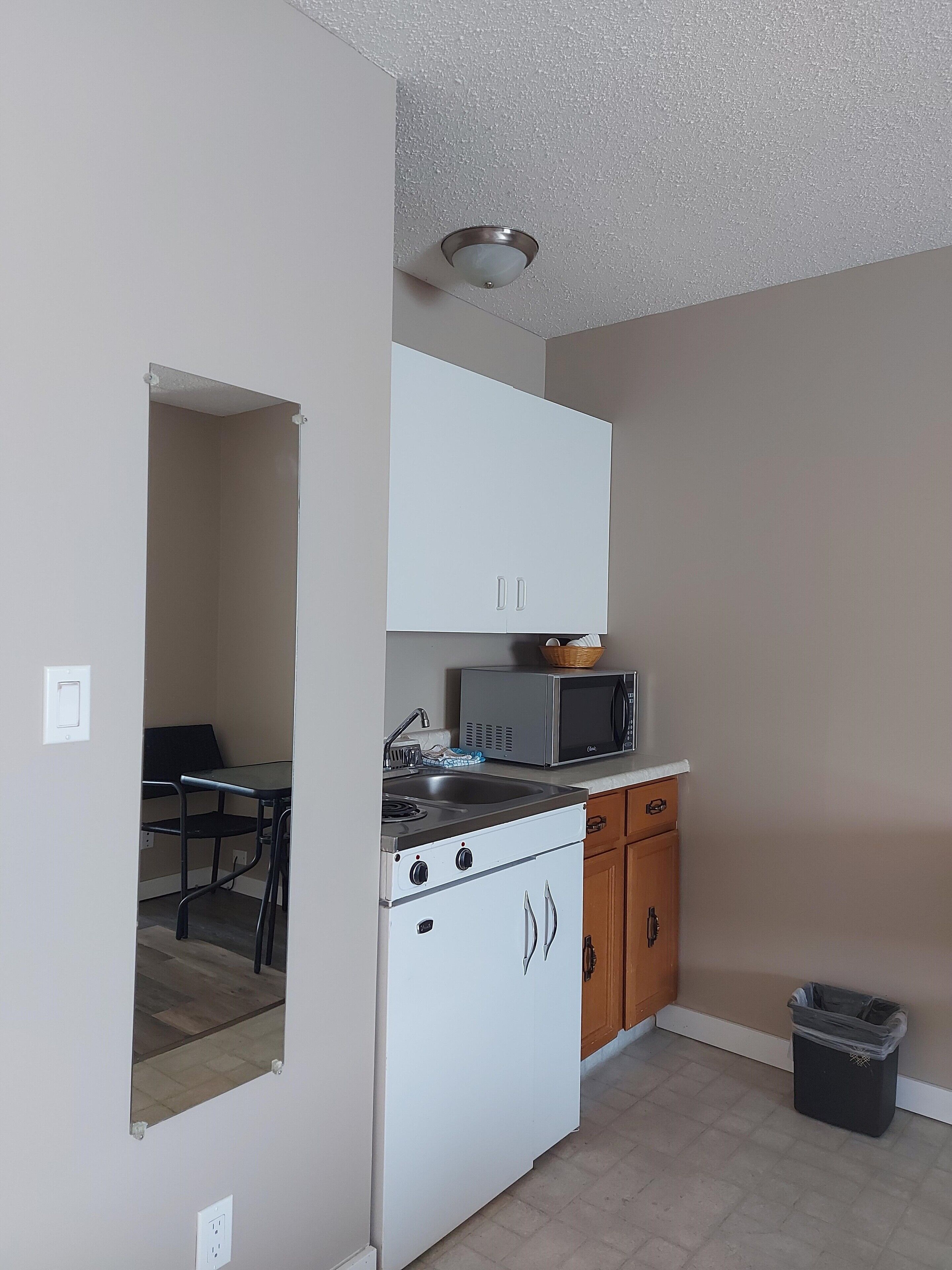 A compact kitchen with white cabinets, a microwave, a stove, and a trash bin.