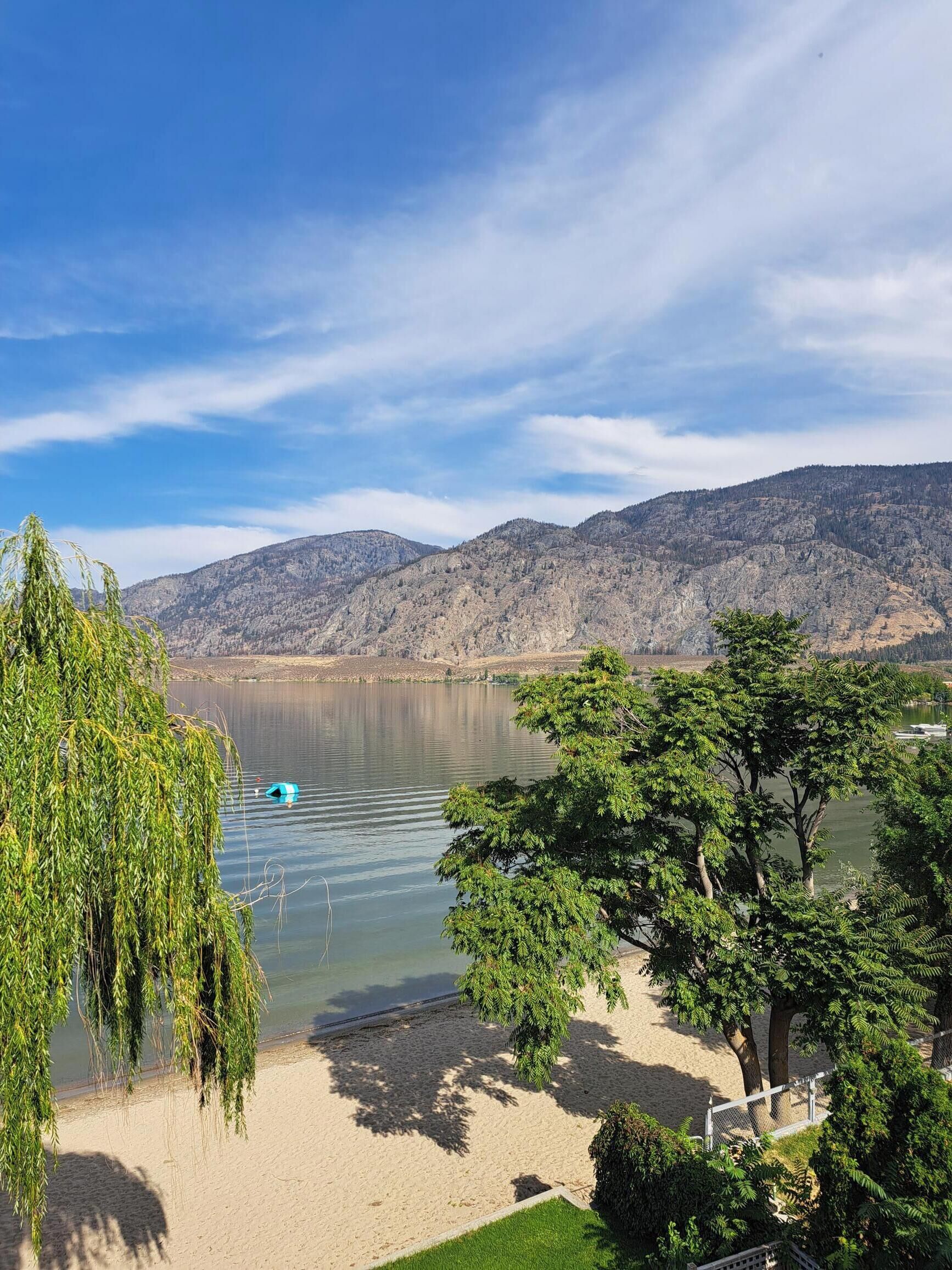 A lakeside view with a sandy beach, trees, and mountains in the background.