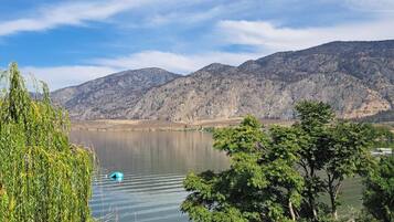 A lakeside view with a sandy beach, trees, and mountains in the background.