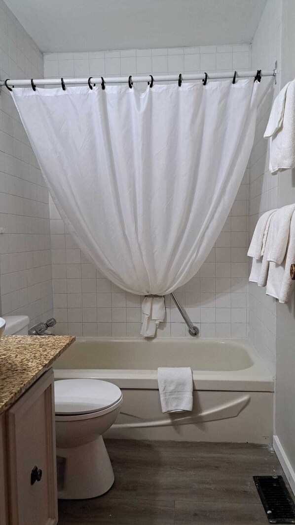 A bathroom with a bathtub, toilet, and a shower curtain. - Richter Pass Beach Resort (Osoyoos)