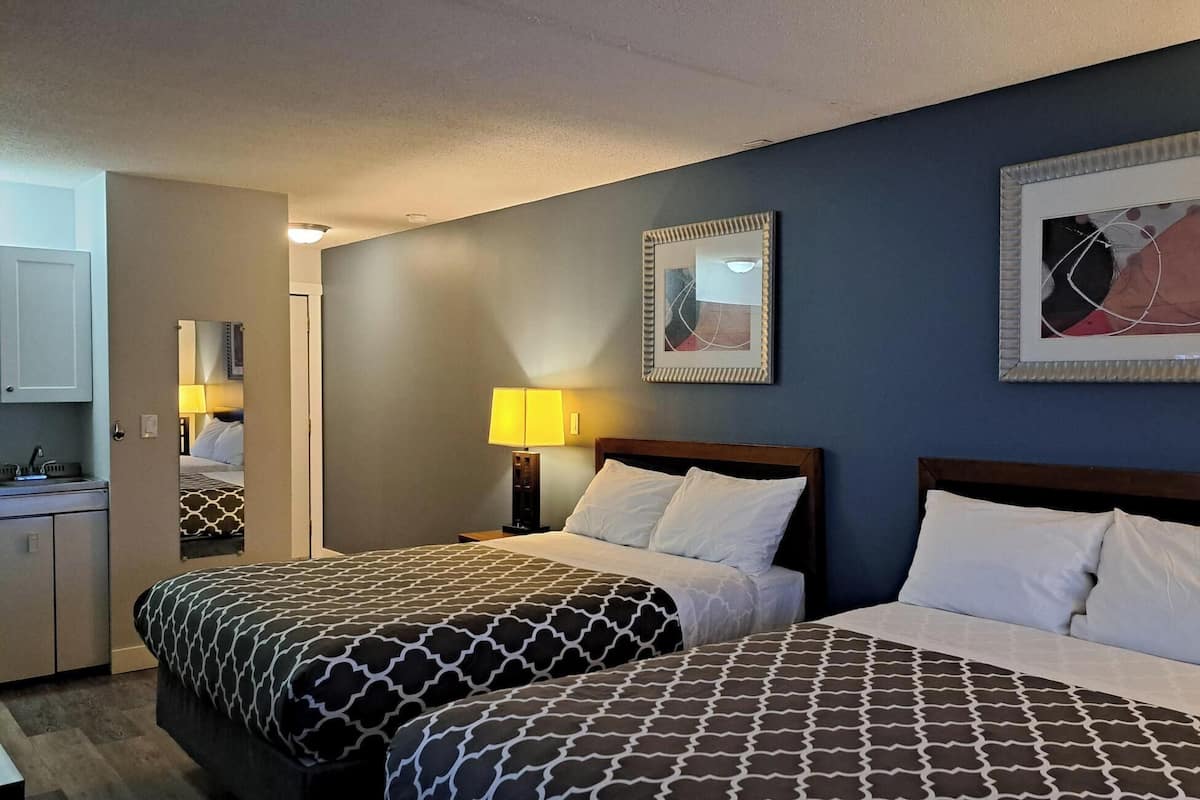 A hotel room with two beds, a desk, a mirror, and two framed pictures on the wall.