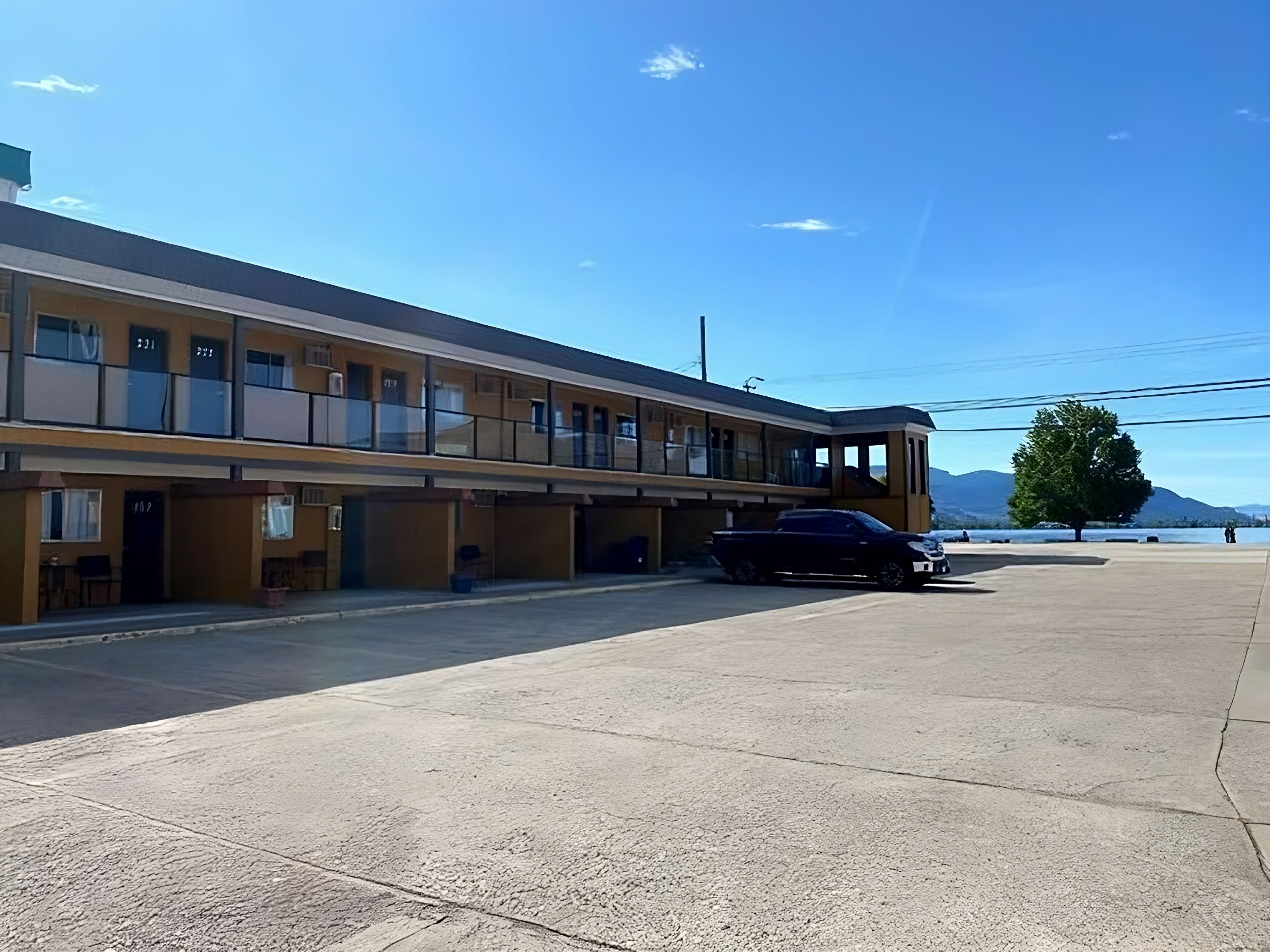 A motel with multiple rooms, a parking area, and a view of mountains.