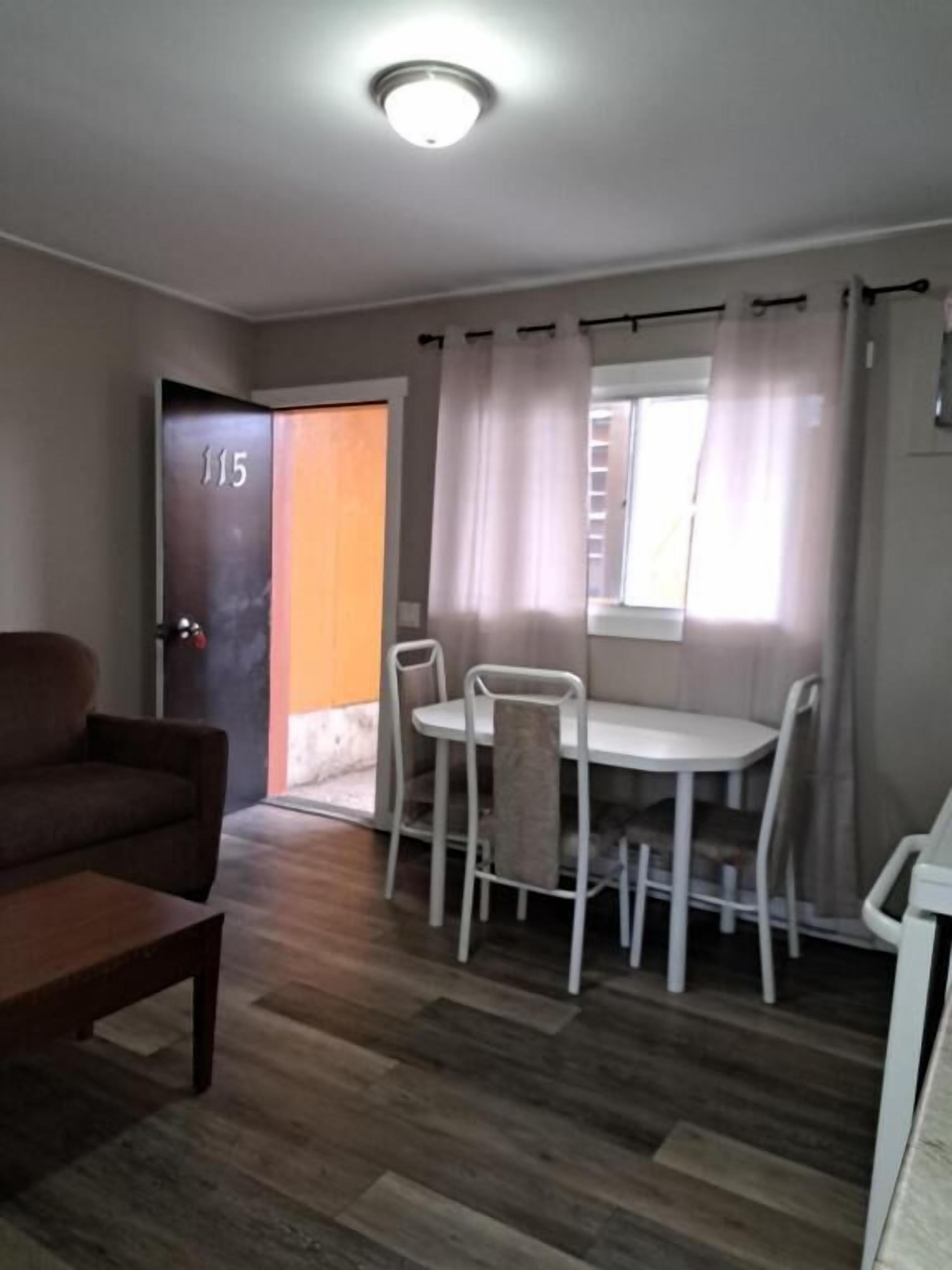 A room with a dining table and chairs, a sofa, and a door marked with the number 115.