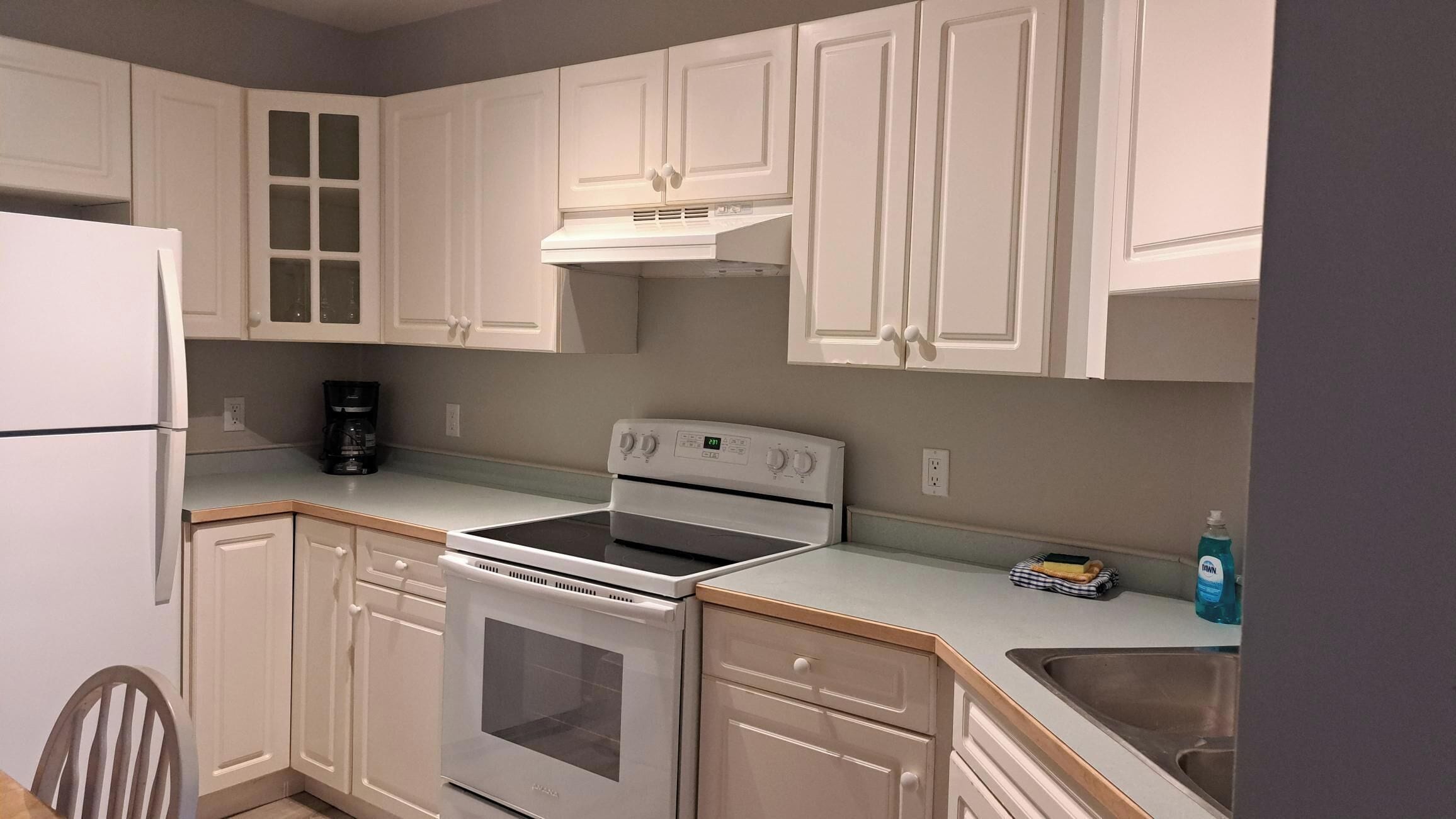 A kitchen with white cabinets, a white stove, and a coffee maker on the counter.