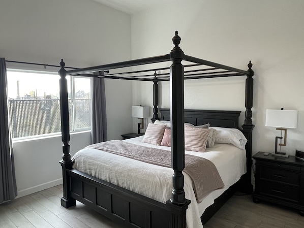 Un lit à baldaquin avec une tête de lit, deux tables de chevet avec des lampes, une fenêtre avec des rideaux et une vue sur l’extérieur.