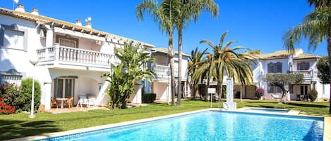 A poolside view of a hotel with a swimming pool, palm trees, and a well-maintained lawn.