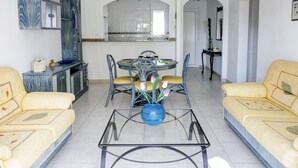 A spacious living room with a dining area, featuring a glass coffee table, yellow sofas, and a modern kitchen with white cabinets. - Lovely apartment for 4 guests with WIFI, pool, A/C, TV and terrace (Denia)