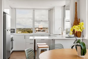 Une cuisine moderne dotée d’une grande fenêtre, de meubles blancs et offrant une vue sur un immeuble situé de l’autre côté de la rue.