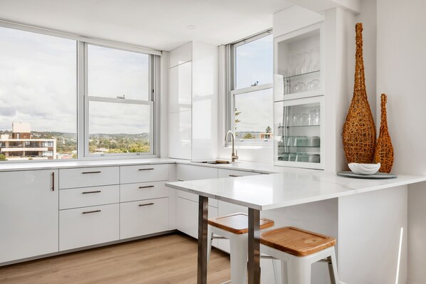 Eine moderne Küche mit weißen Schränken, einer weißen Arbeitsplatte und einem großen Fenster mit Blick auf die Stadt.