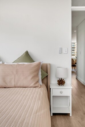 Une chambre à coucher bien rangée, avec un lit, des oreillers, une table de chevet avec une lampe et une commode.