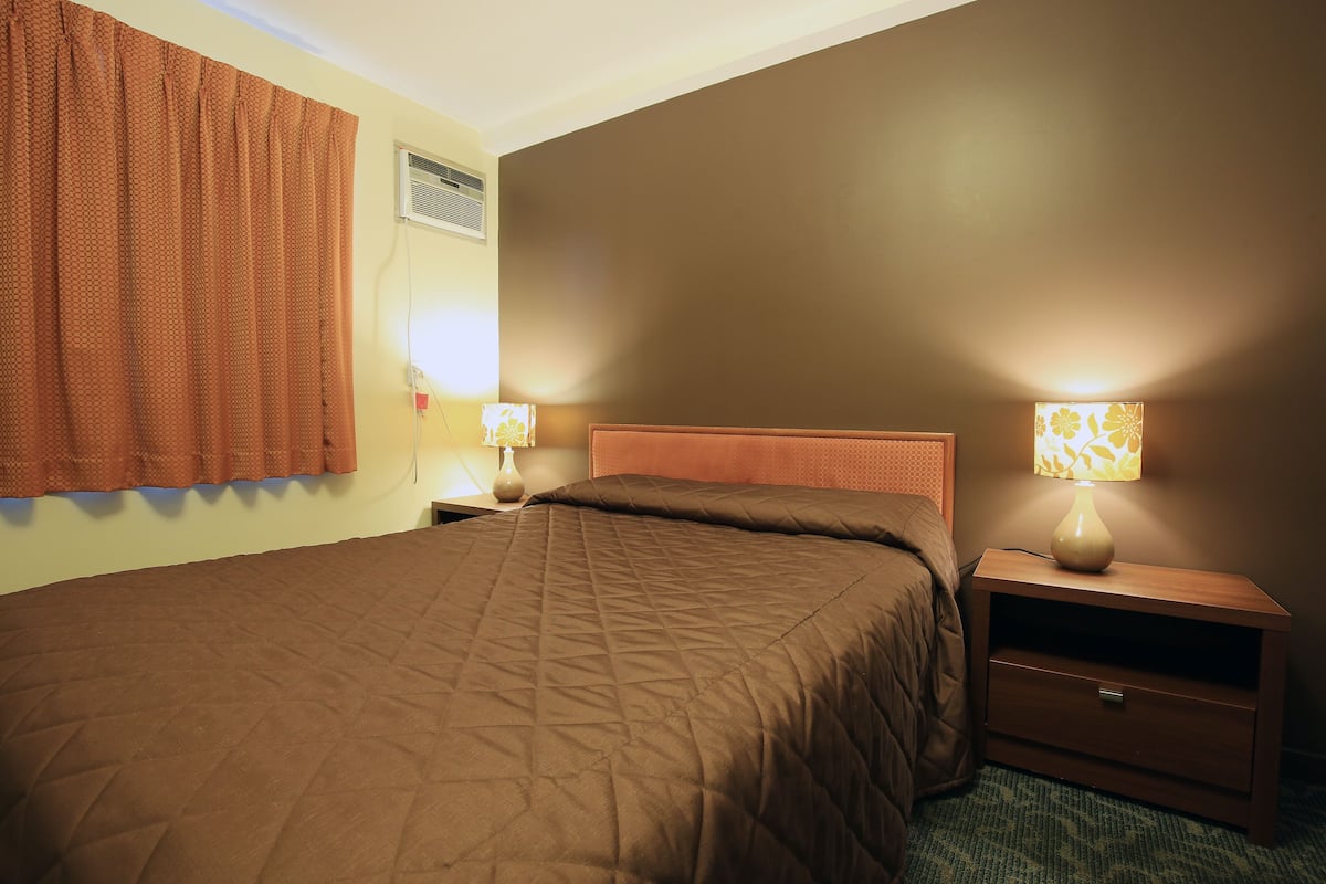 A hotel room with a bed, nightstands, lamps, and a wall-mounted air conditioner.