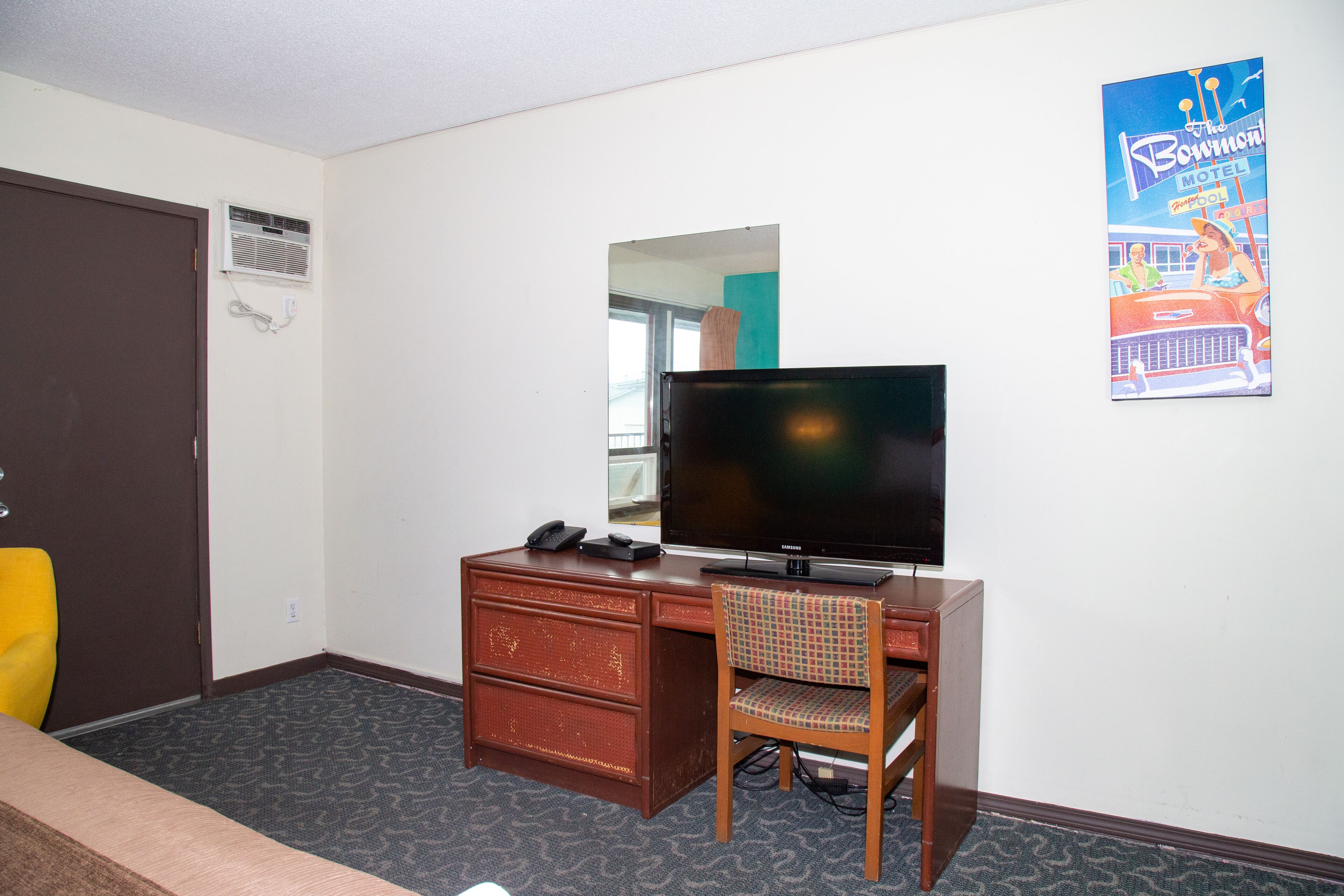Una habitación de hotel con escritorio, silla, televisión y un cartel en la pared.