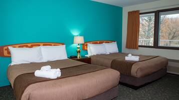 Une chambre d’hôtel avec deux lits, des murs de couleur turquoise et une fenêtre donnant sur des arbres.