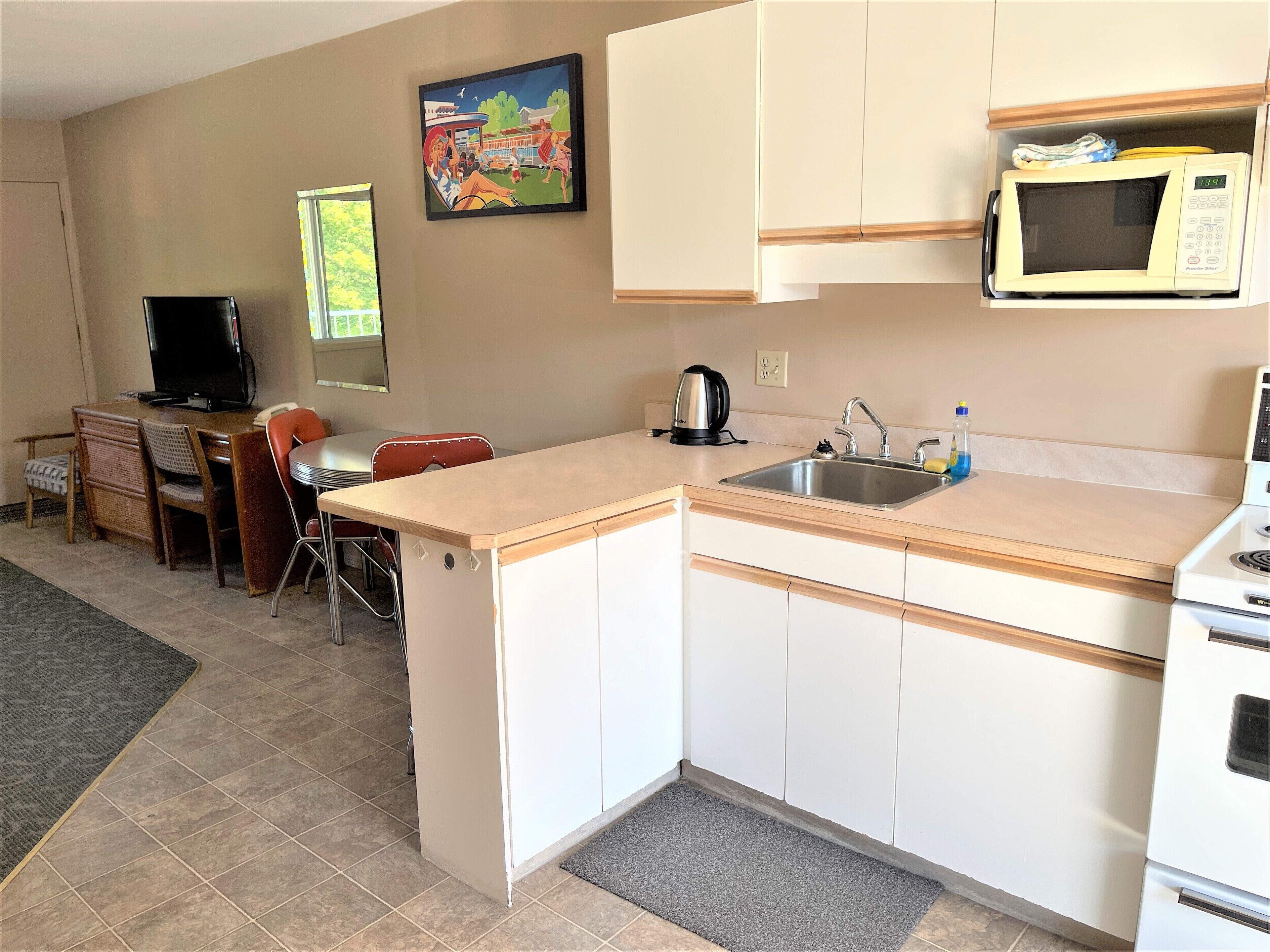 A compact kitchen with a microwave, sink, and a small dining area with a chair and table.