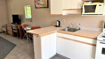 A compact kitchen with a microwave, sink, and a small dining area with a chair and table.