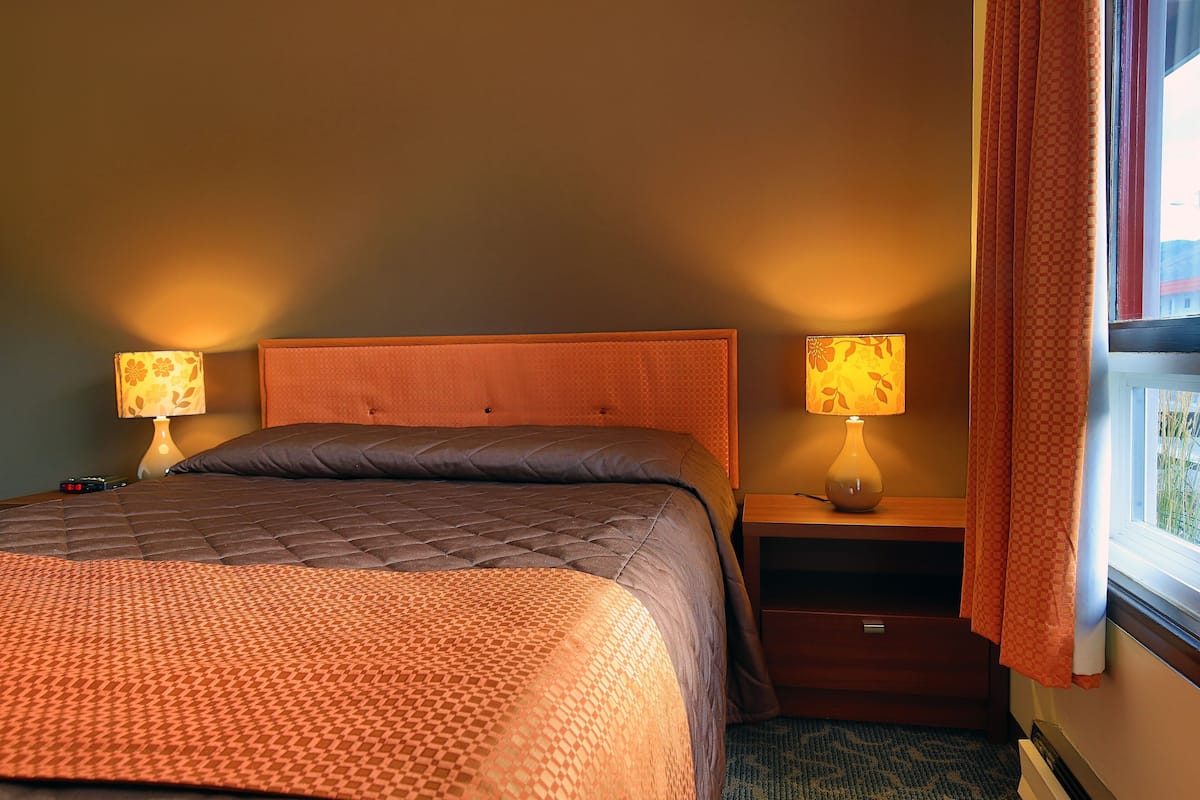 A hotel room with a bed, two bedside lamps, a nightstand, and a window with curtains.