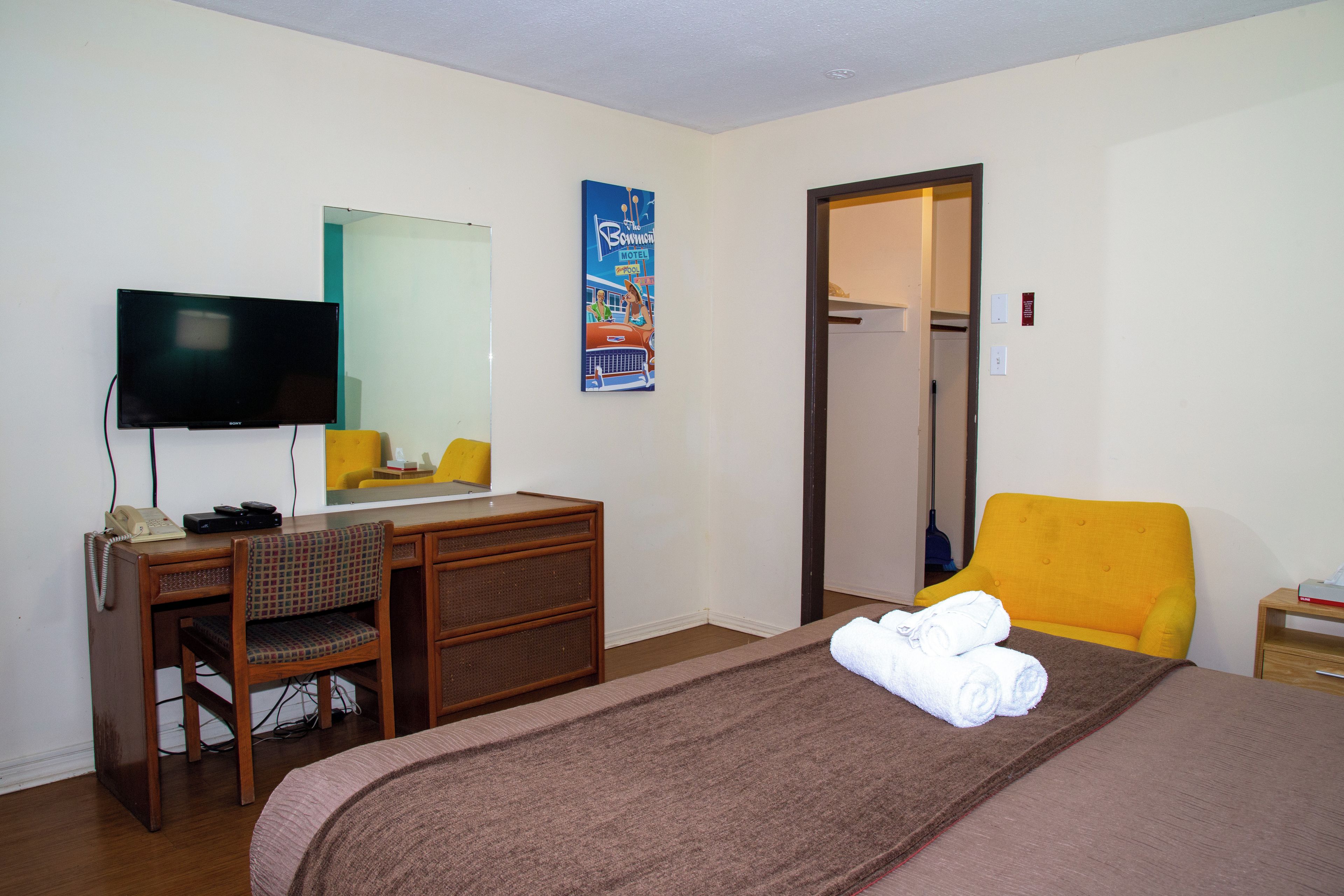 A hotel room with a bed, a desk with a chair, a television, and a door leading to a bathroom.