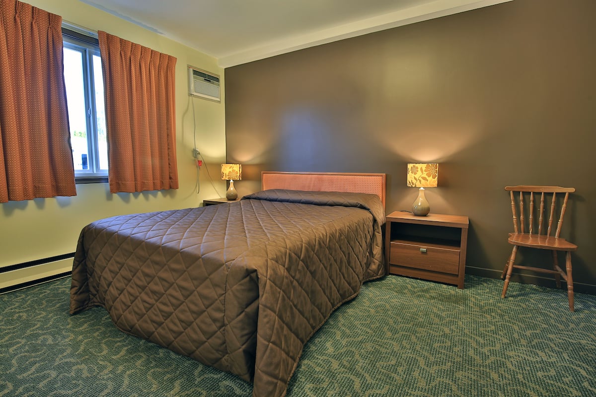 A hotel room with a large bed, two bedside tables with lamps, a wooden chair, and a window with curtains.