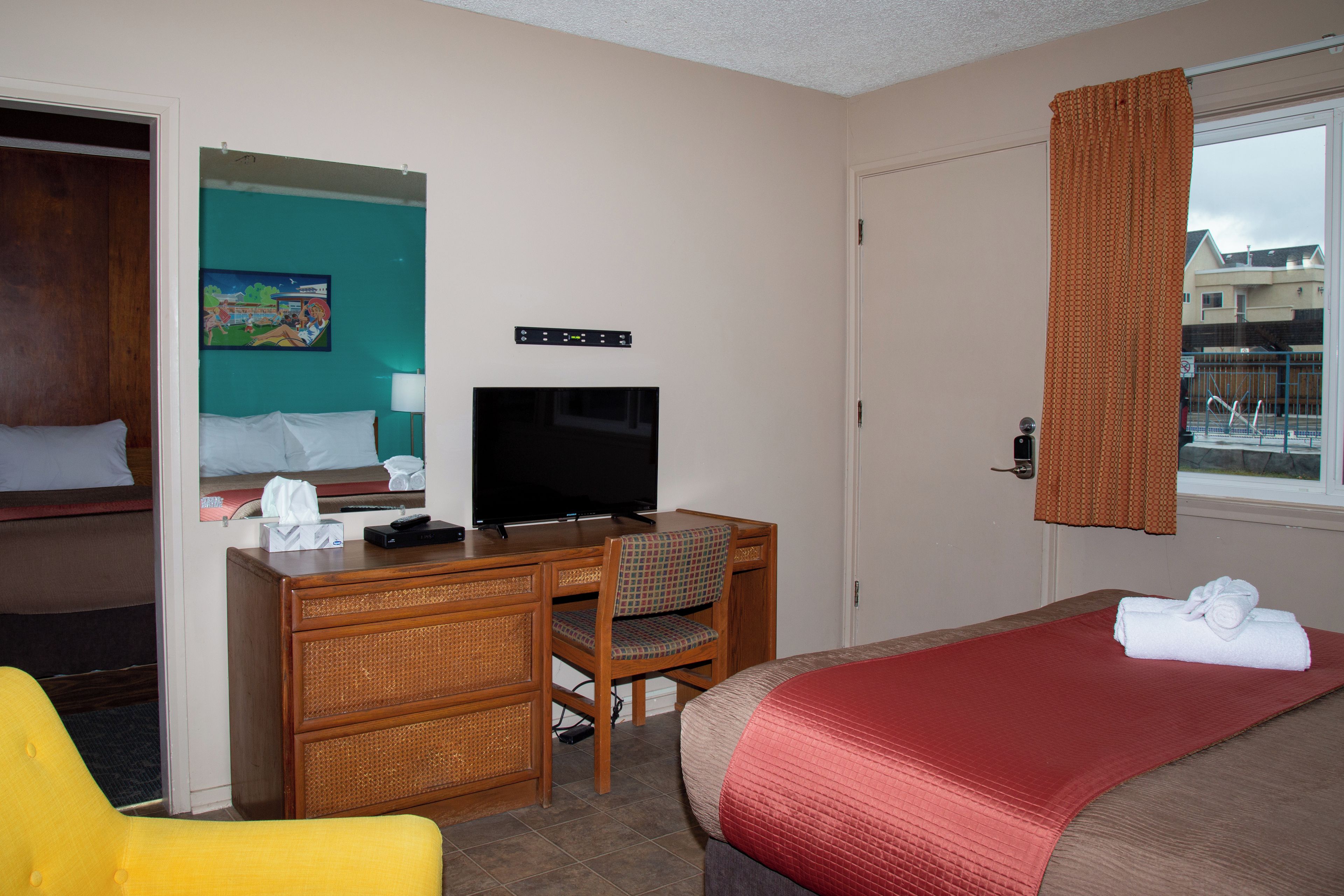 A hotel room with a bed, a desk with a television, a chair, and a window with curtains.