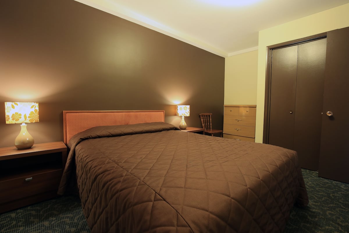 A bedroom with a large bed, two bedside tables with lamps, a dresser, and a wardrobe.