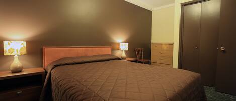 A bedroom with a large bed, two bedside tables with lamps, a dresser, and a wardrobe.