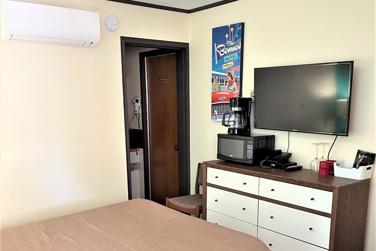 A hotel room with a bed, a dresser, a television, a coffee maker, and a poster on the wall.
