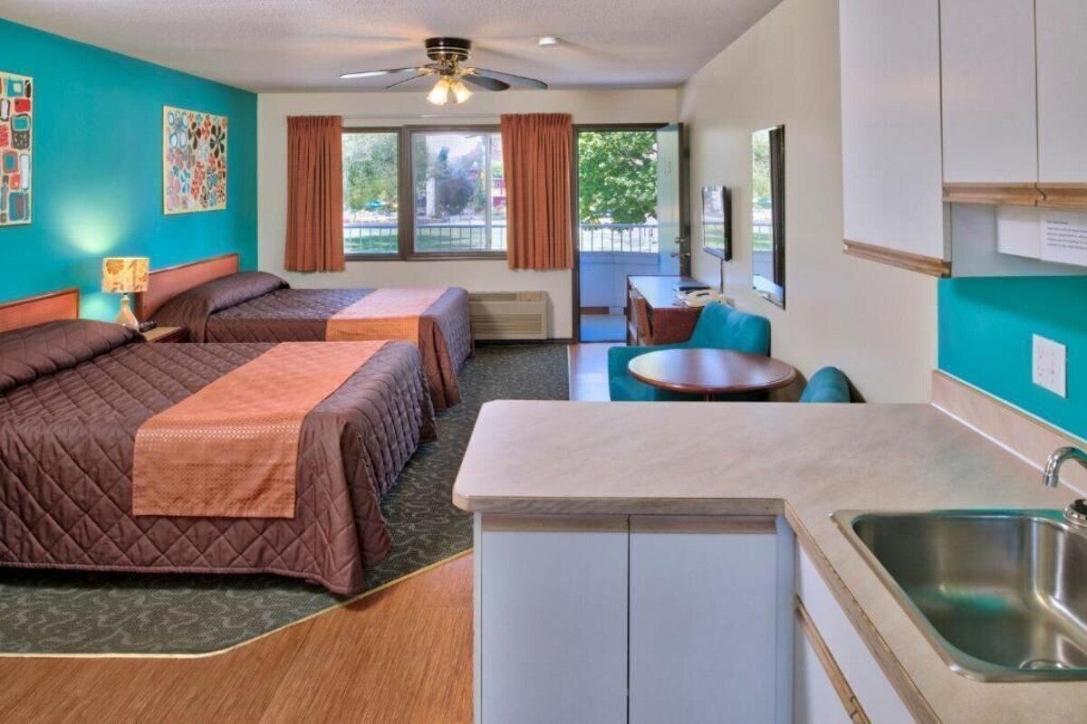 Habitación de hotel con dos camas, kitchenette, zona de comedor y vistas al exterior.