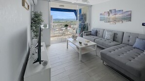 A modern living room with a grey sofa, a white coffee table, and a balcony with a view of the city. - Exceptional Modern Beachfront Escape • XL Pool • In-Unit Laundry • VIP Parking (Carolina)