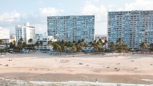A beach with high-rise buildings in the background, palm trees, and clear turquoise water. - Exceptional Modern Beachfront Escape • XL Pool • In-Unit Laundry • VIP Parking (Carolina)