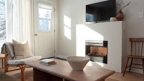 En stue med pejs, et tv hængt over, og et hyggeligt siddeområde med sofa og stole.