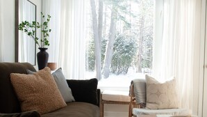 En hyggelig stue med en sofa, et lille bord og et vindue med gardiner.