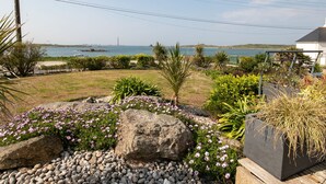 Une propriété située sur la côte, offrant une vue sur la mer, un phare et un jardin agrémenté de rochers et de fleurs.