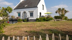 Une maison blanche avec un toit gris, un parasol vert et un palmier dans la cour.