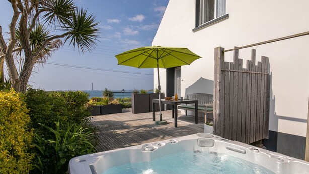Un jacuzzi avec vue sur la mer, une terrasse en bois et une table avec des chaises.