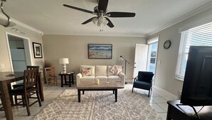 Ein Wohnzimmer mit Deckenventilator, einer Essecke mit Tisch und Stühlen, einem Sofa, einem Couchtisch und einem Fernseher.