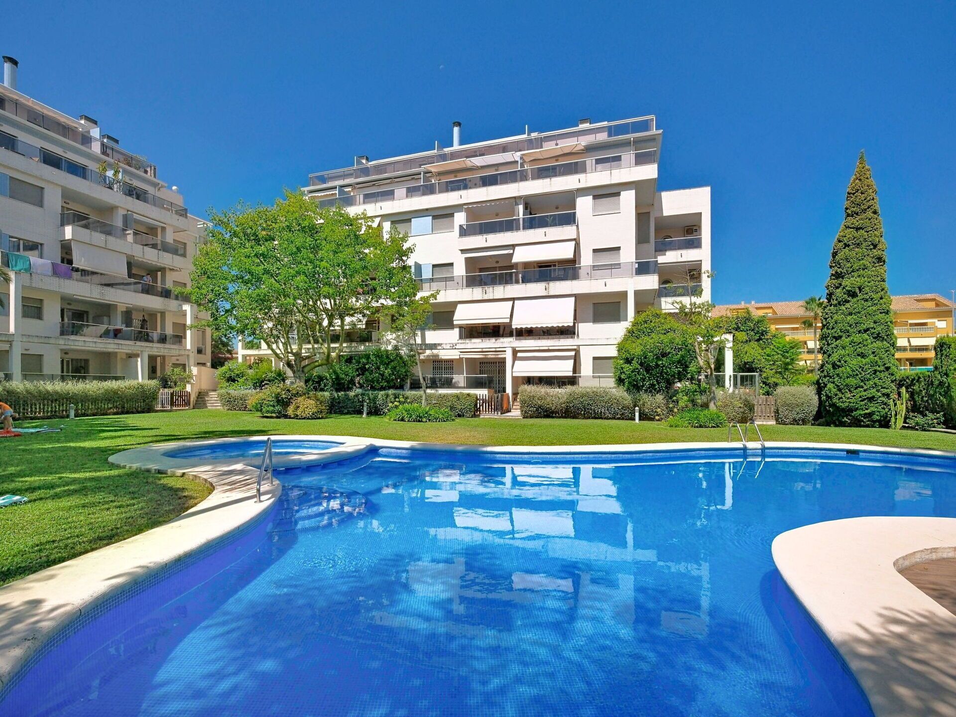 Edificio residencial con piscina, rodeado de vegetación y cielo despejado.