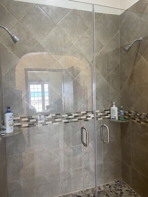 Une douche avec une porte en verre, un mur carrelé et une petite étagère où sont rangés les produits de toilette.