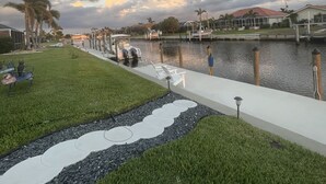A waterfront property with a grassy area, a pathway with stepping stones, and a dock with boats. - Punta Gorda Isles Jewel with 45ft dock,just4minutes from Fishville and downtown. (Punta Gorda)