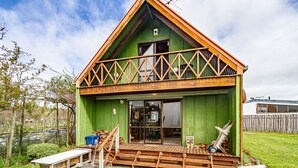 Uma casa de madeira verde com um alpendre de madeira, um banco e uma pilha de lenha.