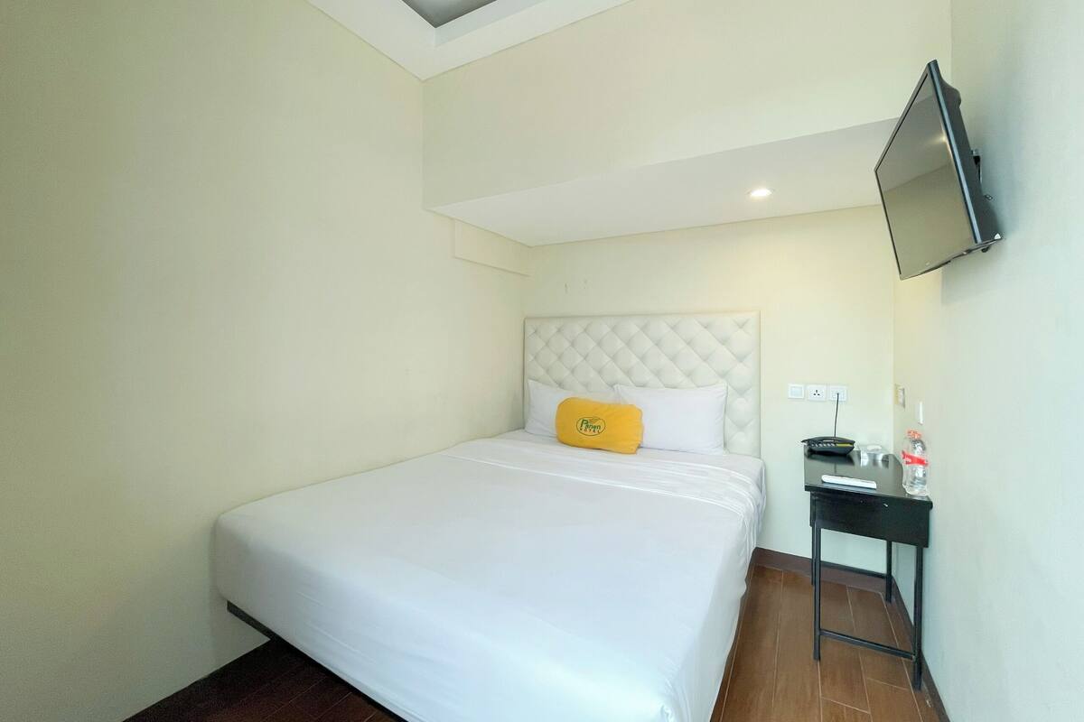 A hotel room with a bed, a small desk, a television mounted on the wall, and a ceiling light.