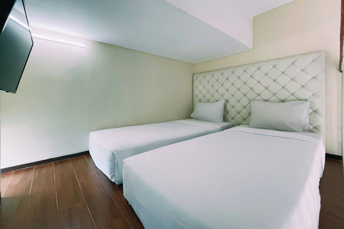 A hotel room with two beds, a flat-screen TV mounted on the wall, and a wooden floor.