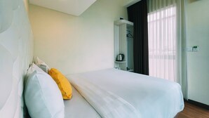 Una habitación de hotel con cama, armario, espejo y ventana con cortinas.