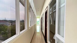 Un pasillo largo y estrecho con grandes ventanales en un lado y puertas en el otro, que conduce a un espacio interior luminoso.
