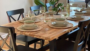 A dining table set with plates, bowls, and wine glasses, surrounded by chairs. - Large 5BR House w/ Backyard, Deck, and Patio (Princeton)