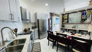 A modern kitchen with stainless steel appliances, a dining area with red upholstered chairs, and a bar area with glassware.