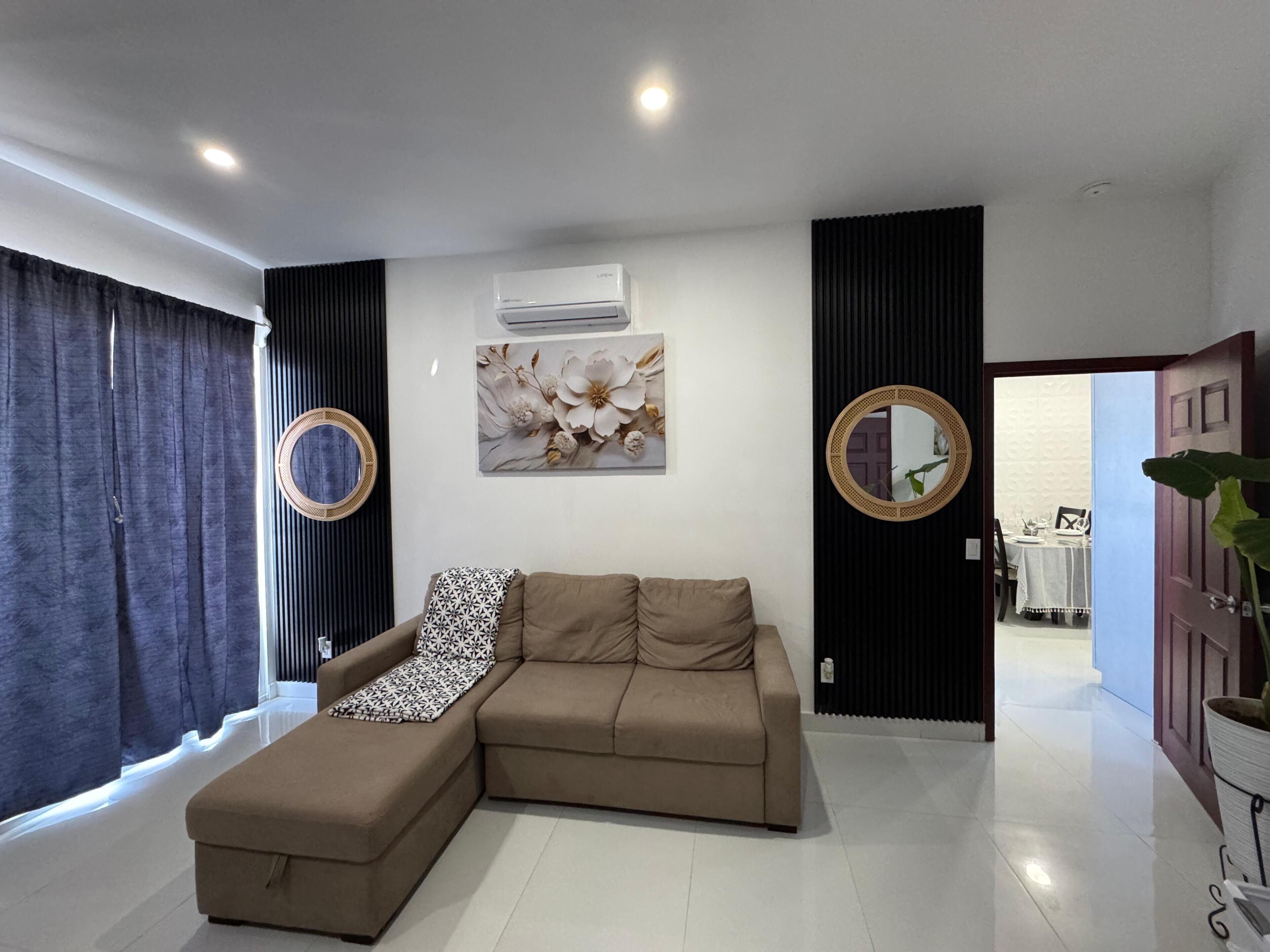 A modern living room with a sectional sofa, two wall-mounted air conditioning units, and decorative mirrors.