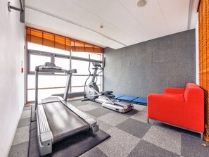 Een sportschool met een loopband, elliptische trainer en een rode bank.