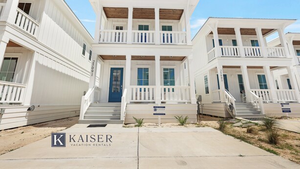 Un immeuble blanc à deux étages, avec une porte bleue et une enseigne indiquant « Kaiser Vacation Rentals ».
