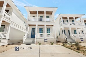 Un edificio blanco de dos pisos con una puerta azul y un letrero que indica 'Kaiser Vacation Rentals'.